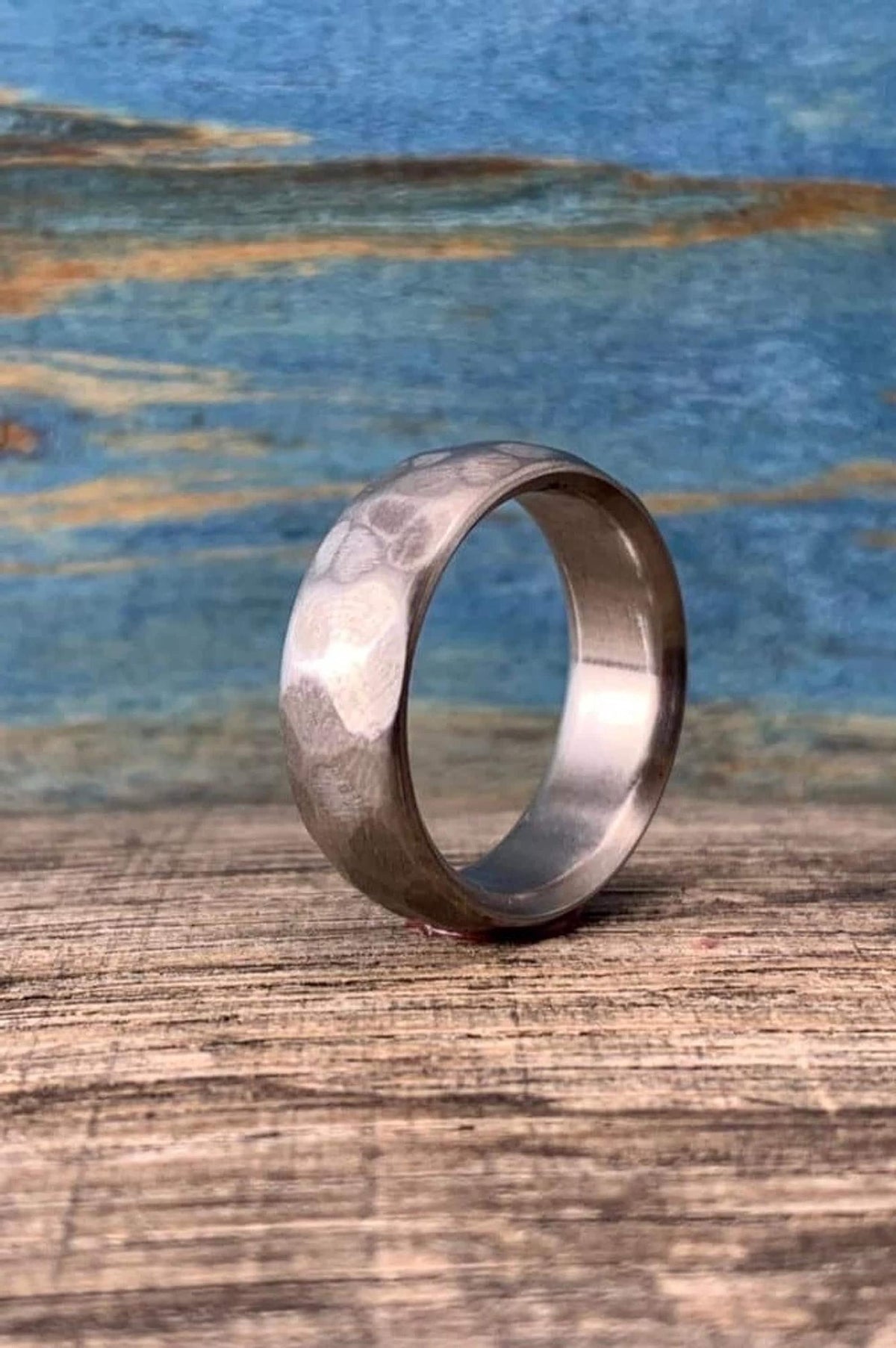 The hammered metal ring is positioned upright, showing its textured outer surface and smooth interior band on a wooden table. __etsy:8394300760