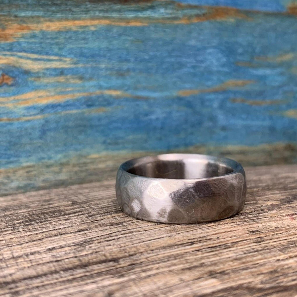 The hammered metal ring rests flat on its side on a rustic wooden surface. __etsy:8394273430