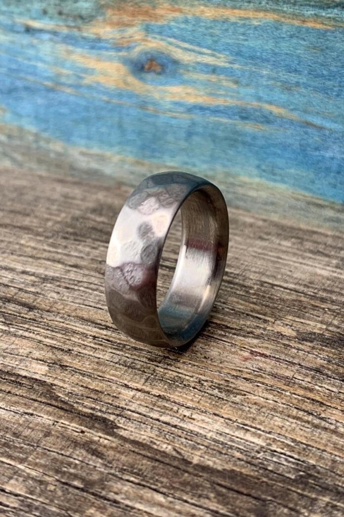 A silver metal ring with a hammered surface stands upright, angled slightly toward the camera on a wooden board. __etsy:8442181549