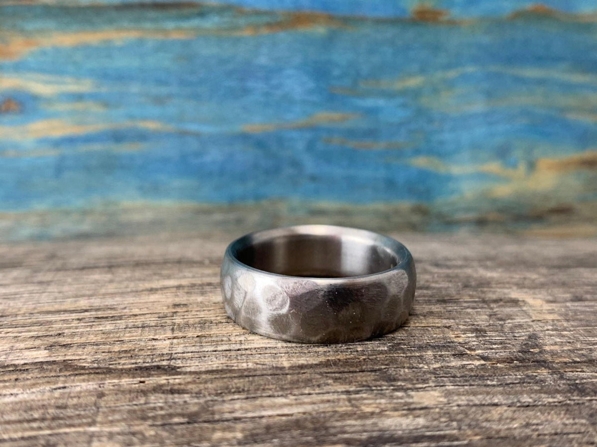 The textured metal band rests flat on a wooden surface against a blue textured backdrop. __etsy:8442155067