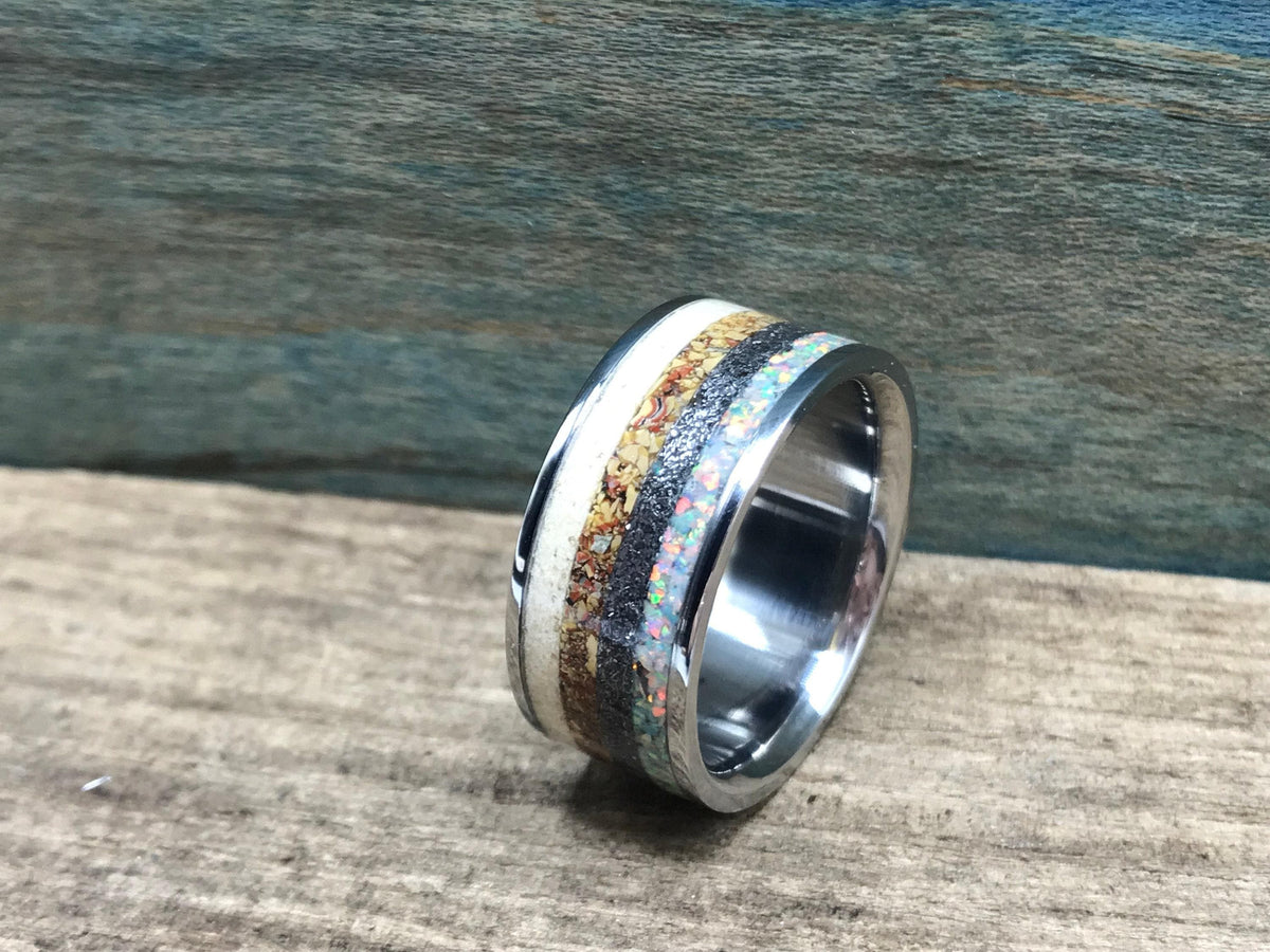 A silver-toned ring with a central band of black, brown, white, and iridescent opal-like segments, viewed from a slight angle on a wooden surface. __etsy:8342872602
