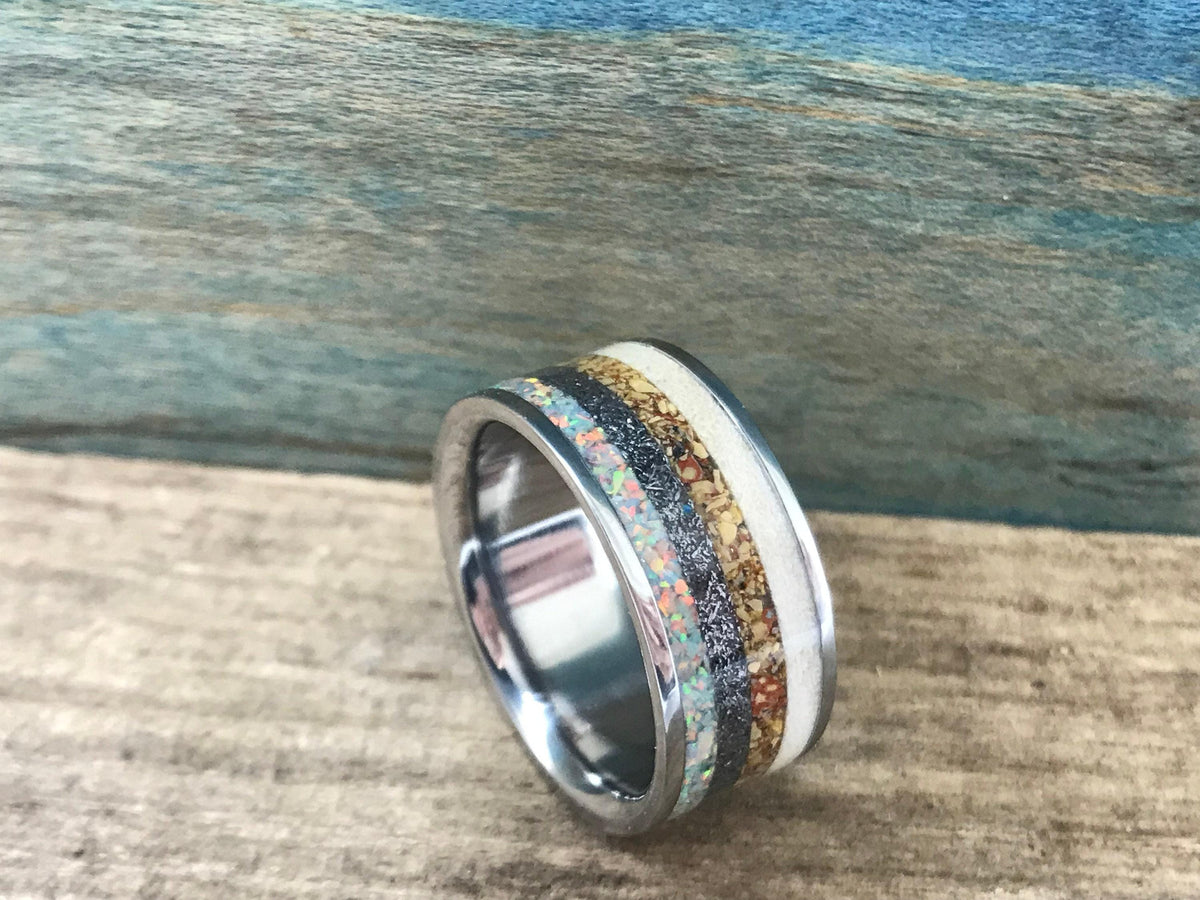 A silver-toned ring with a central band of black, brown, white, and iridescent opal-like segments, viewed from a slight angle on a wooden surface. __etsy:8390755769