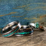 A wedding band set featuring two meteorite rings with bright teal opal inlays and a matching engagement ring with a teal moissanite stone resting on a rustic wooden surface. __etsy:8425545013