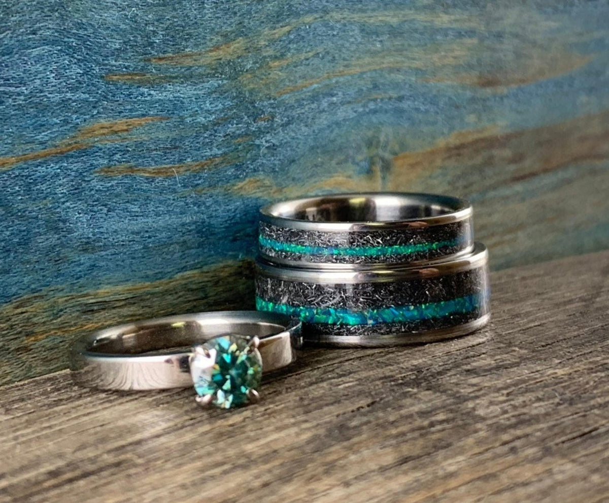 Two meteorite and teal opal rings stacked vertically beside a single teal moissanite ring on a textured wooden plank. __etsy:8425545239