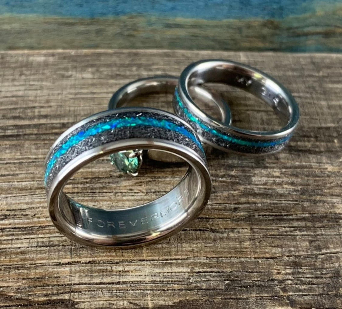Two meteorite wedding bands with teal opal inlays, displaying an engraved inscription inside the inner band. __etsy:8377671600