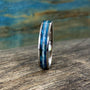 A silver-colored ring with a central inlay of blue wood and white pearl, viewed from a slight angle on a wooden surface.