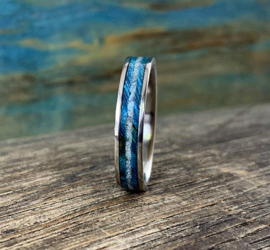 A silver-colored ring with a central inlay of blue wood and white pearl, viewed from a slight angle on a wooden surface.