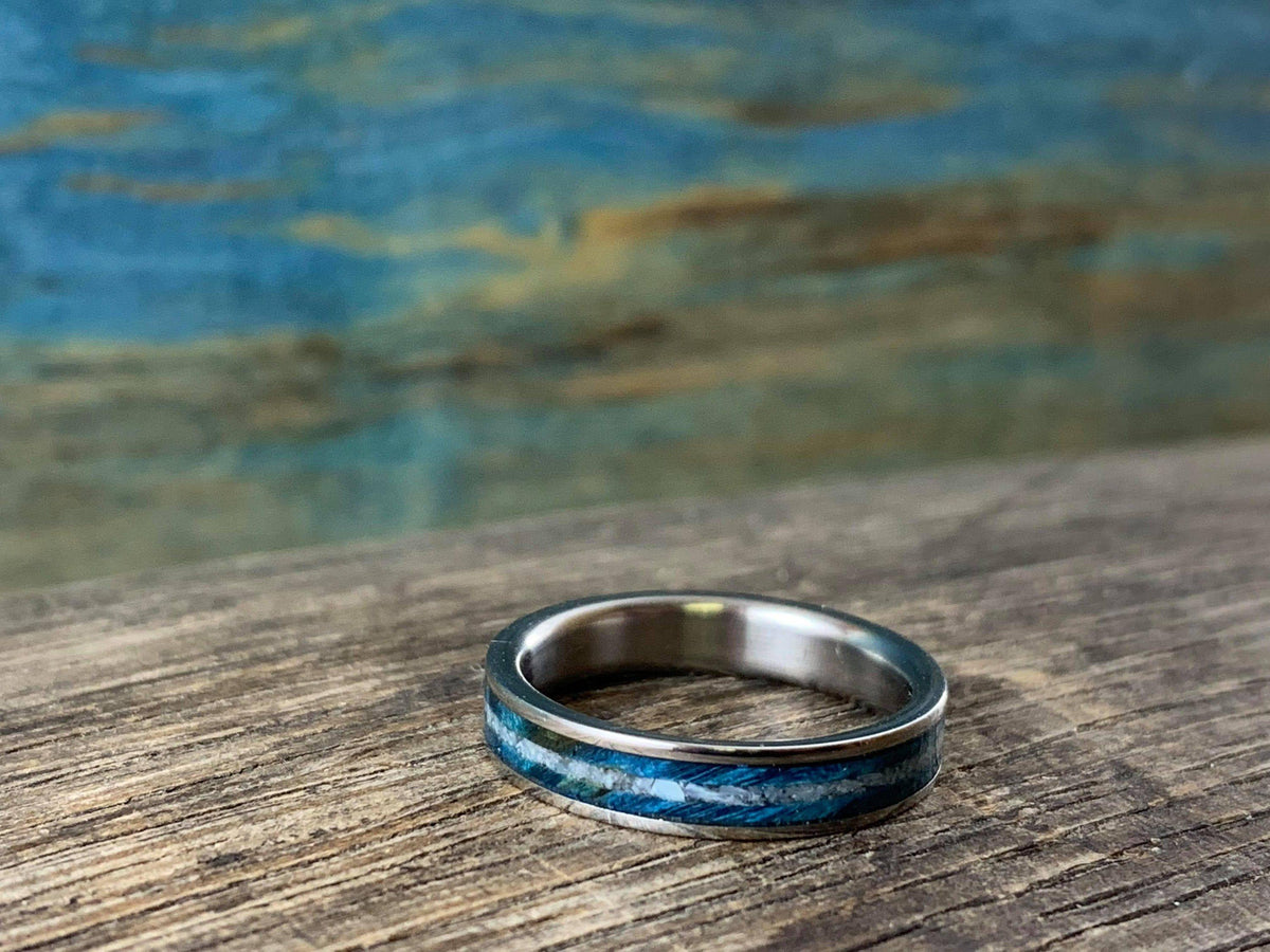 A silver-colored ring with a blue wood and white pearl inlay, viewed from a slightly elevated angle on a wooden surface.