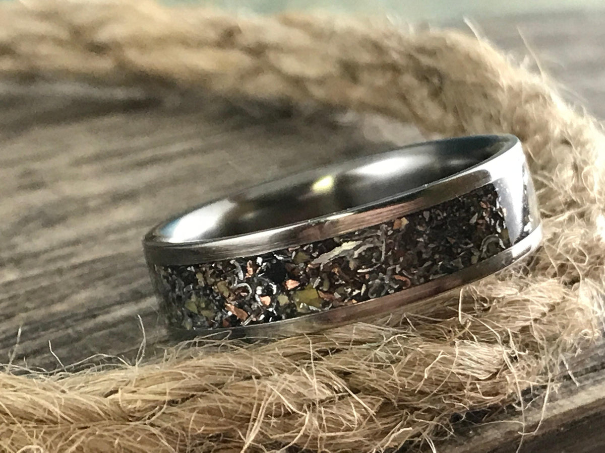 A silver-colored ring with a dark, textured inlay band rests on a thick, braided rope.