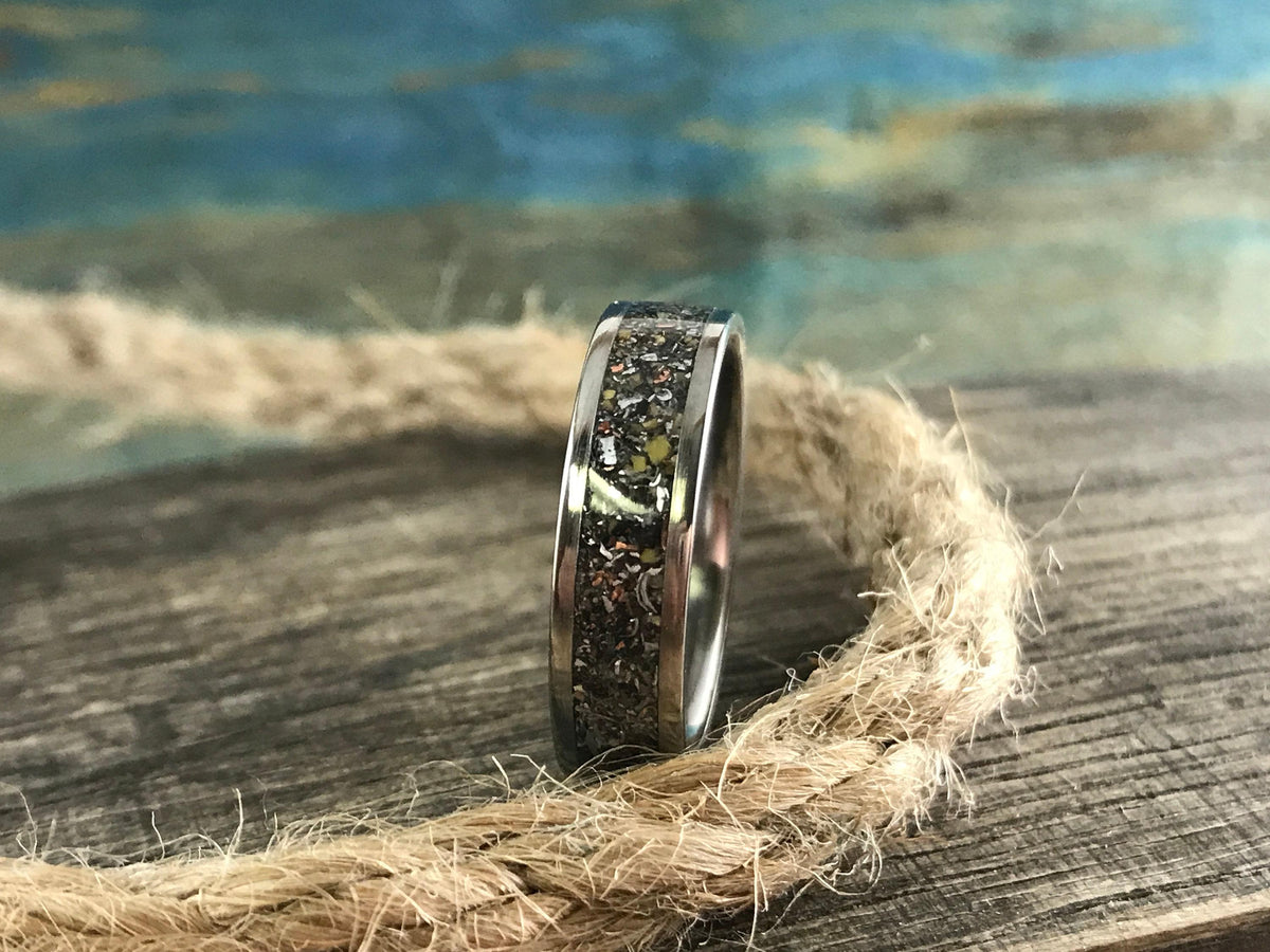A silver-colored ring with a dark, textured inlay band is positioned upright on a thick, braided rope.