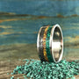 A silver ring with green, yellow, and black inlay bands stands upright on a pile of small green malachite chips.