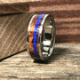 A silver-colored ring with a central band of brown wood and a thin blue stripe, resting on a wooden surface.