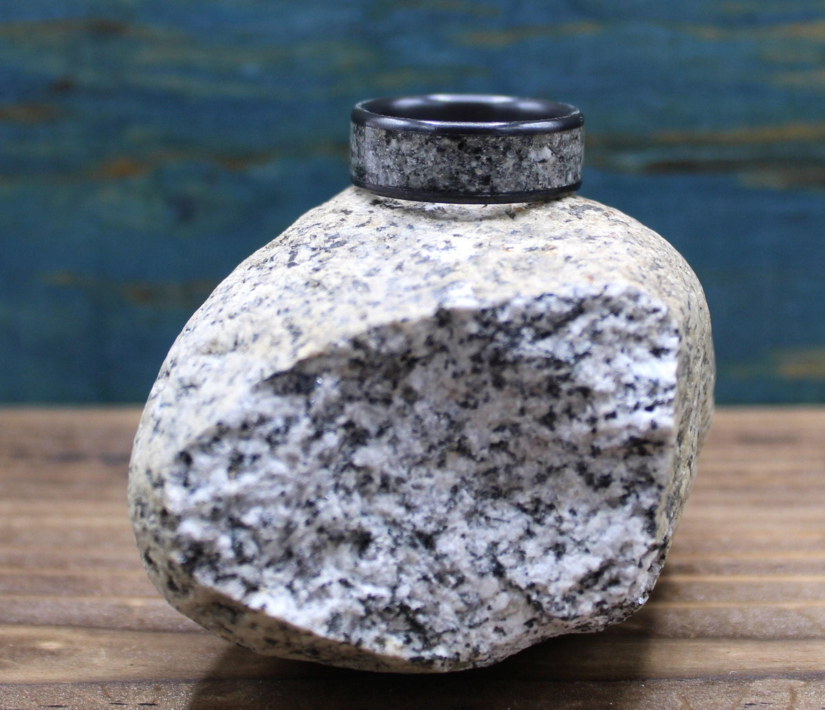 A black ring with a light gray, speckled granite inlay sits on top of a large, light gray granite rock.