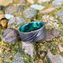 A wide, flat, patterned metal ring with a bright green interior sits on mossy rocks.