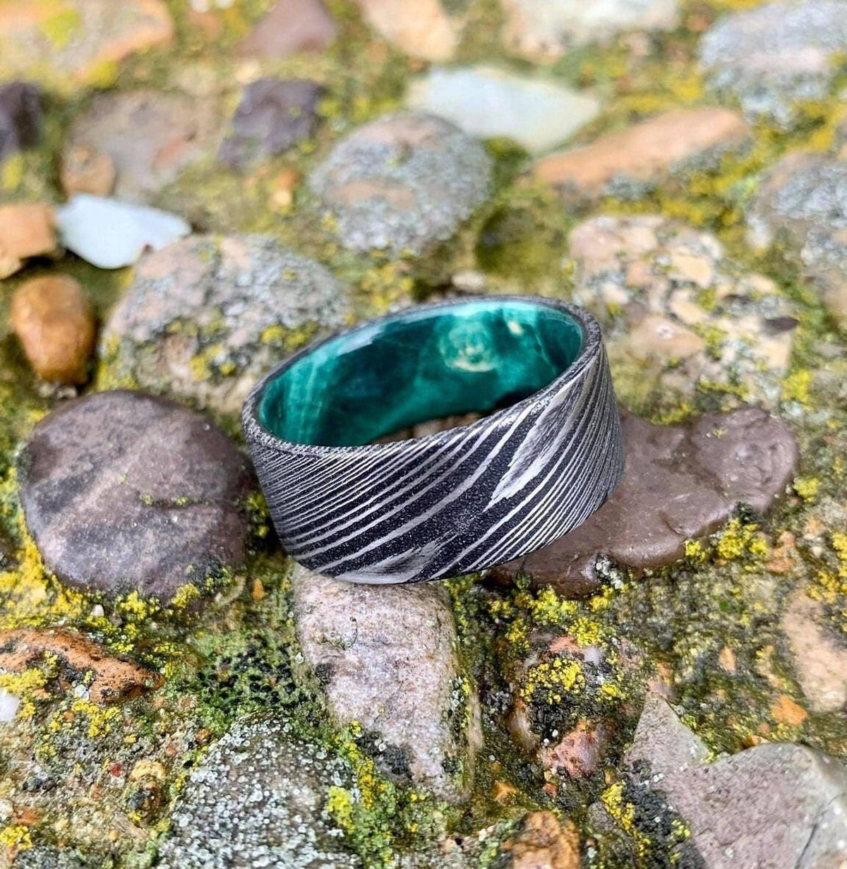 A wide, flat, patterned metal ring with a bright green interior sits on mossy rocks.