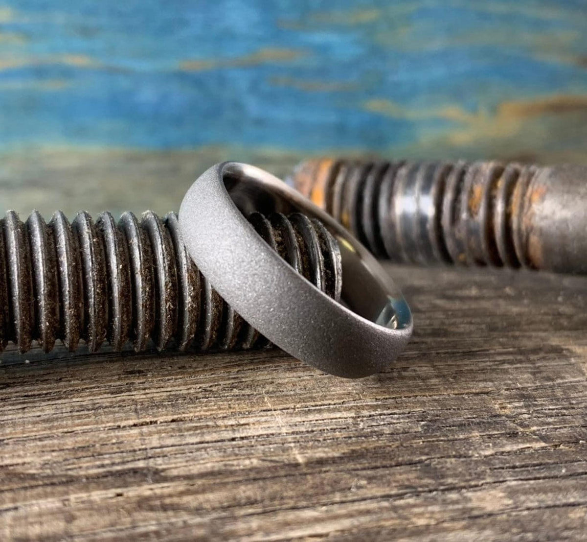 Handcrafted sandblasted titanium ring angled against dark steel bolt