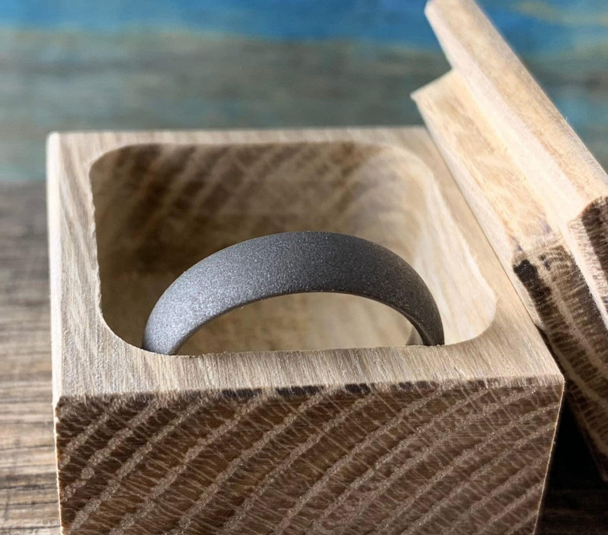 Sandblasted titanium wedding band nestled inside open handcrafted oak ring box