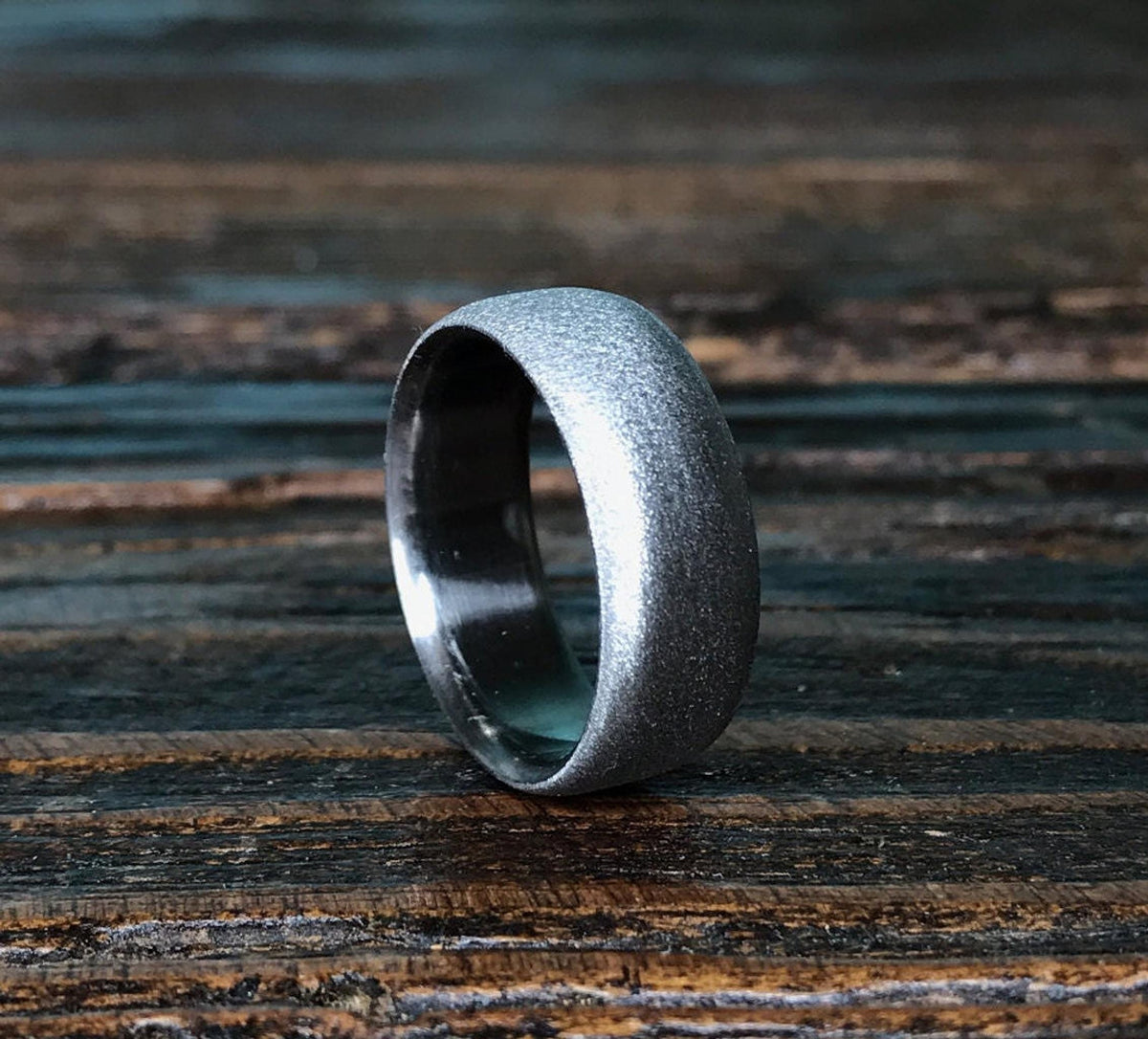 A silver-colored ring with a brushed exterior and a smooth interior, angled on a dark wooden surface.