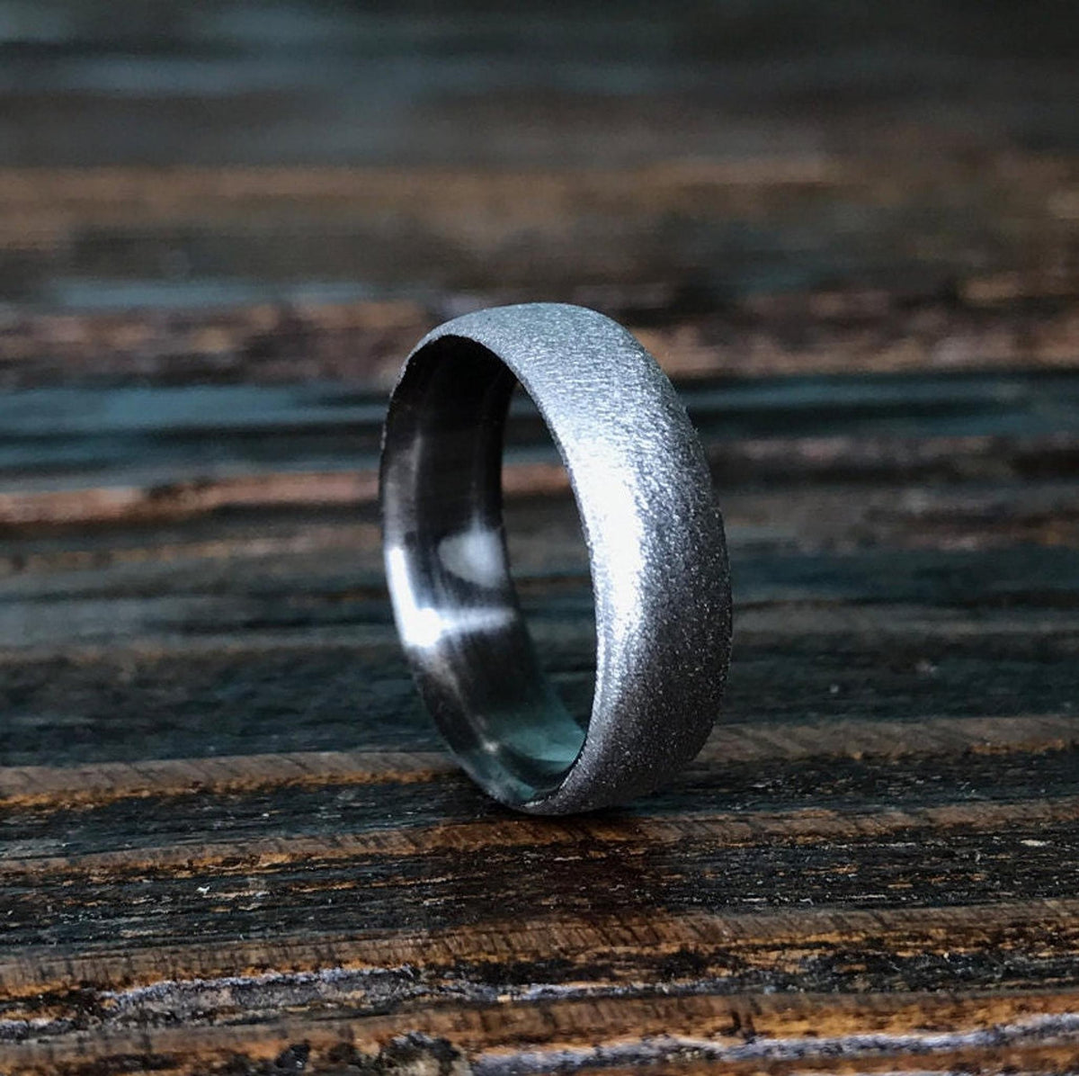 A silver-colored ring with a textured exterior and a smooth interior, lying on a dark wooden surface.