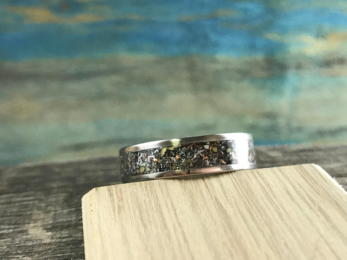 A silver-colored ring with a dark, textured inlay band is centered on a light-colored wooden block.