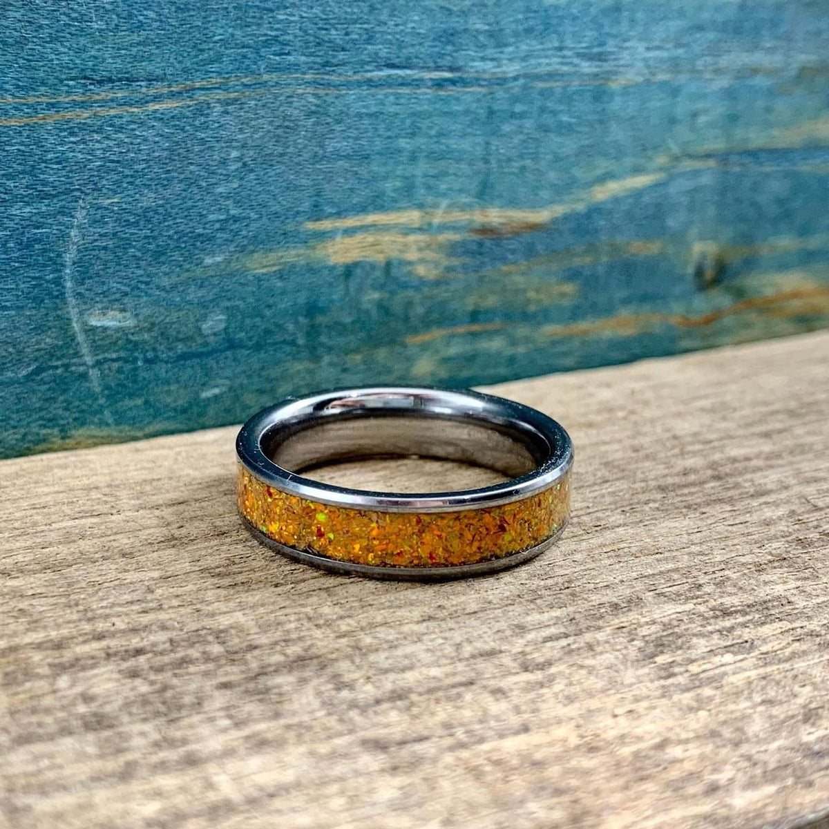 A silver-toned ring with an orange glittery inlay, centered on a wooden surface with a blue background.