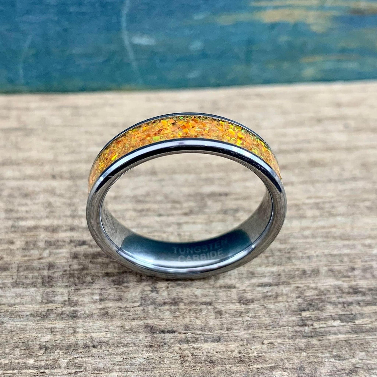 A silver-toned ring with an orange glittery inlay, angled slightly to the right on a wooden surface with a blue background.