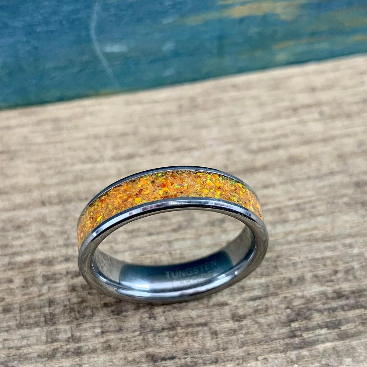 A silver-toned ring with an orange glittery inlay, viewed from above on a wooden surface with a blue background.