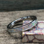 A silver ring with a white opal inlay sits on a wooden surface next to a block of red and white patterned wood.