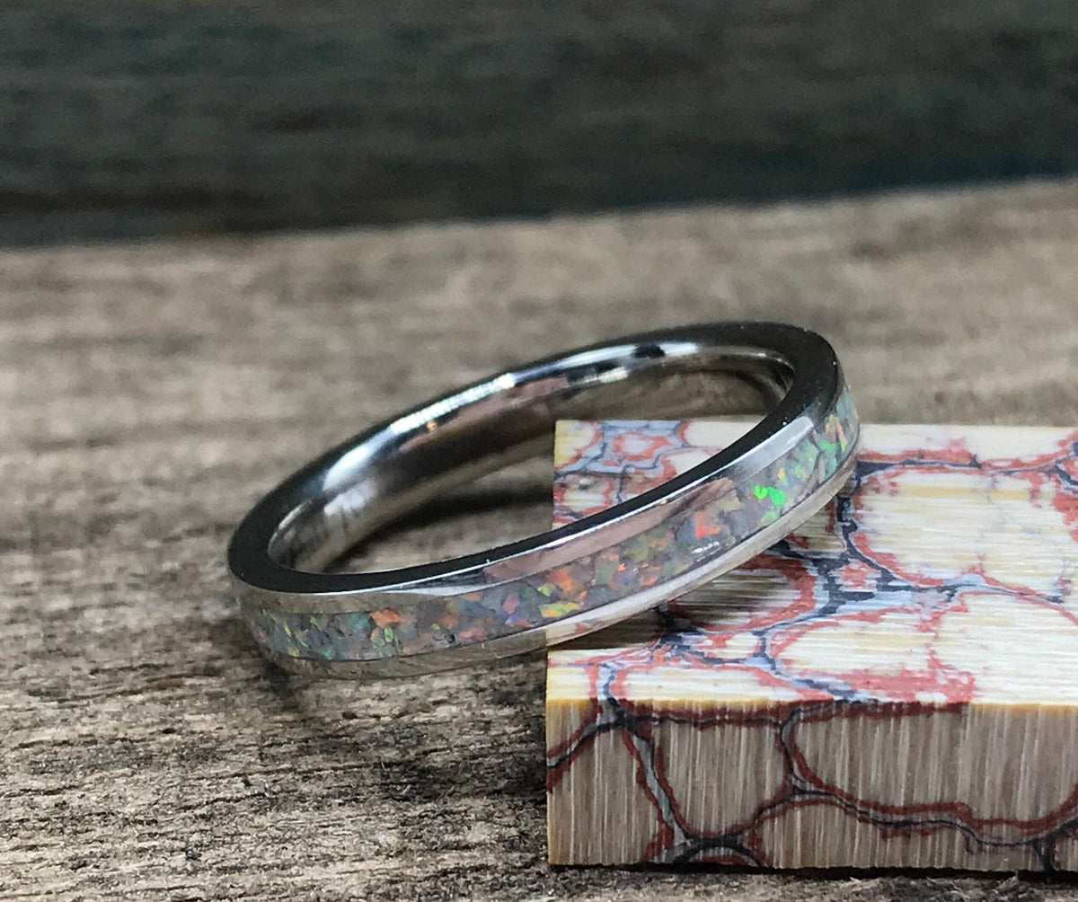 A silver ring with a white opal inlay sits on a wooden surface next to a block of red and white patterned wood.