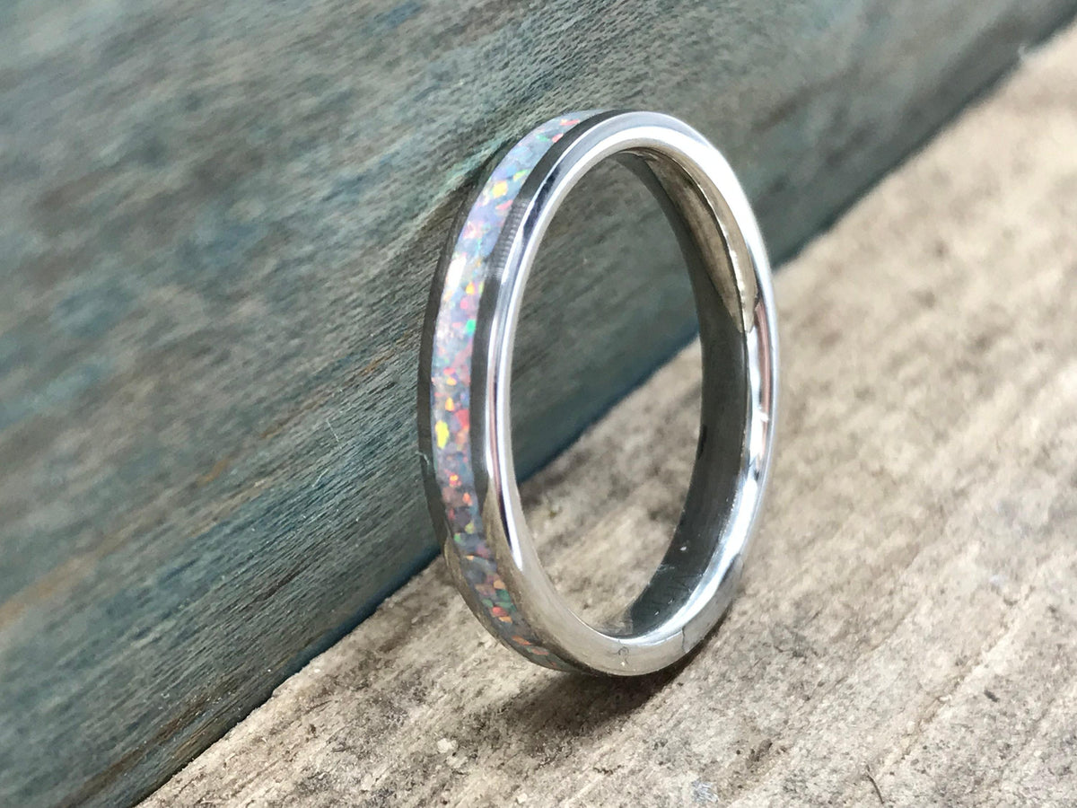 A silver ring with a white opal inlay is angled on a wooden surface, with a blue-painted wood background.