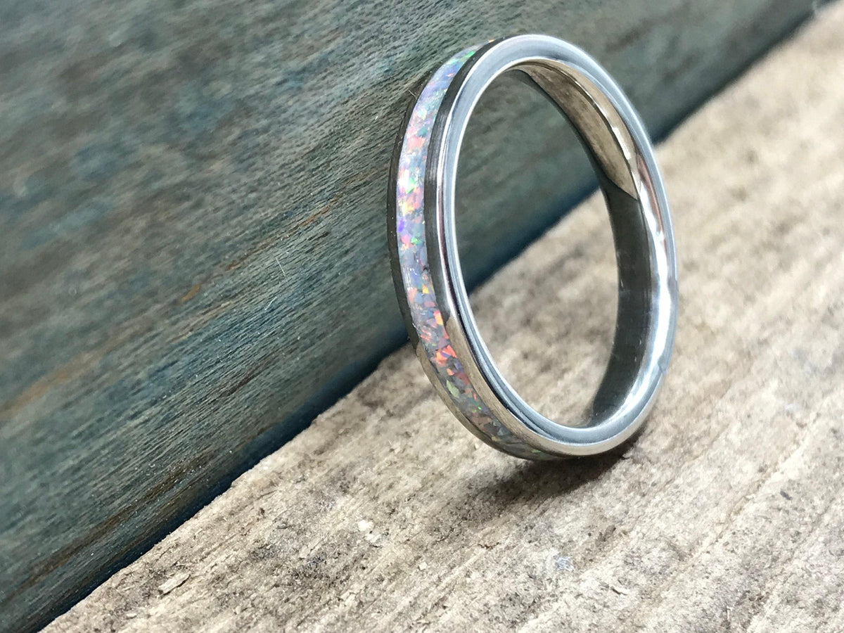 A silver ring with a white opal inlay is placed on a wooden surface, with a blue-painted wood background on the left.