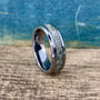 A silver-colored ring with a central band of light green, textured material, set against a wooden surface with a blue background.