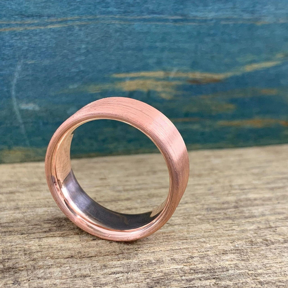 A brushed copper ring with a rounded interior, angled to show the dark interior, on a wooden surface.