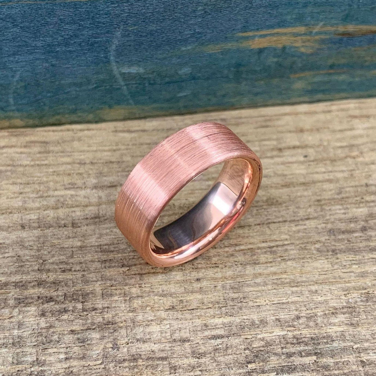 A brushed copper ring with a rounded interior, slightly angled on a wooden surface against a blue background.