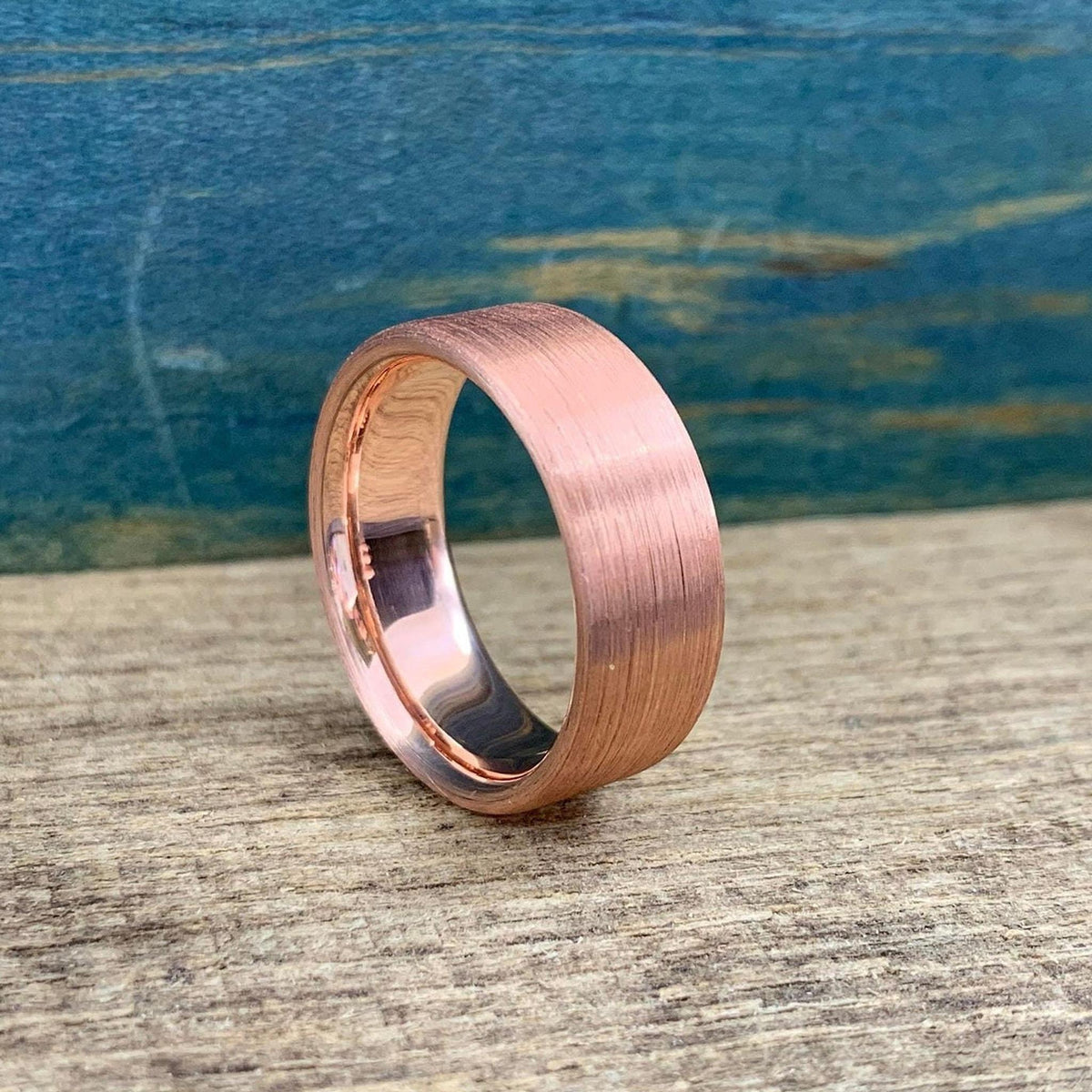 A brushed copper ring with a rounded interior, shown from a slightly elevated angle on a wooden surface.