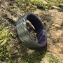 A dark gray Damascus steel ring with a purple interior sits on a mossy log.