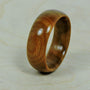 A smooth, polished, light brown wooden ring with visible grain stands upright on a light wooden surface.
