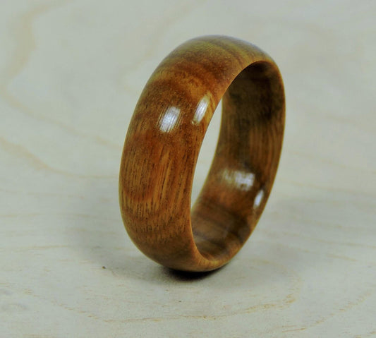 A smooth, polished, light brown wooden ring with visible grain stands upright on a light wooden surface.