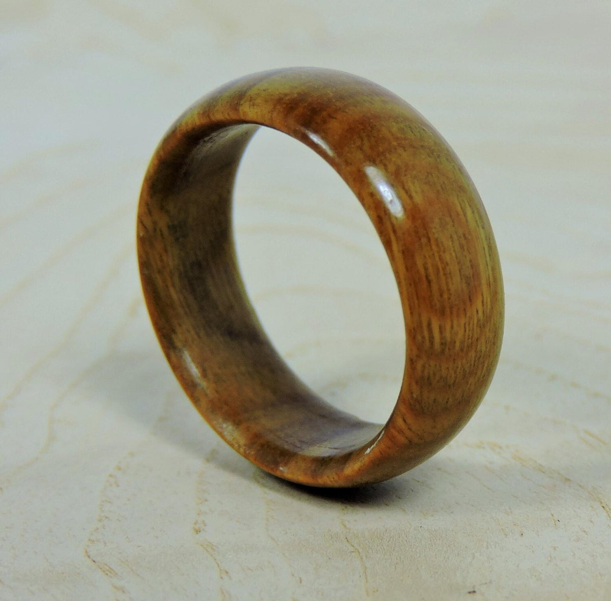 A smooth, polished, light brown wooden ring with visible grain stands upright, angled slightly to the left, on a light wooden surface.