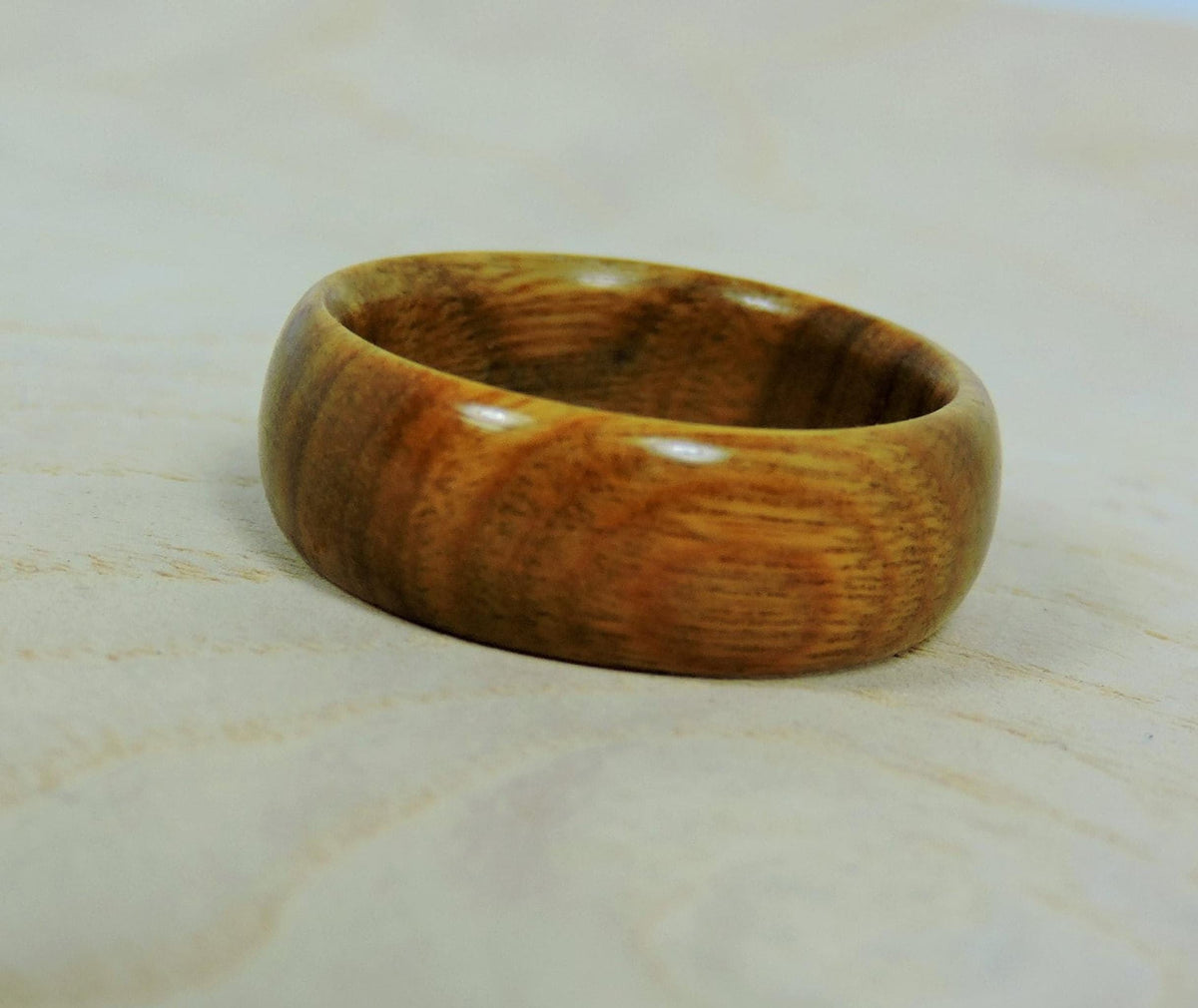 A smooth, polished, light brown wooden ring with visible grain lies flat on a light wooden surface.