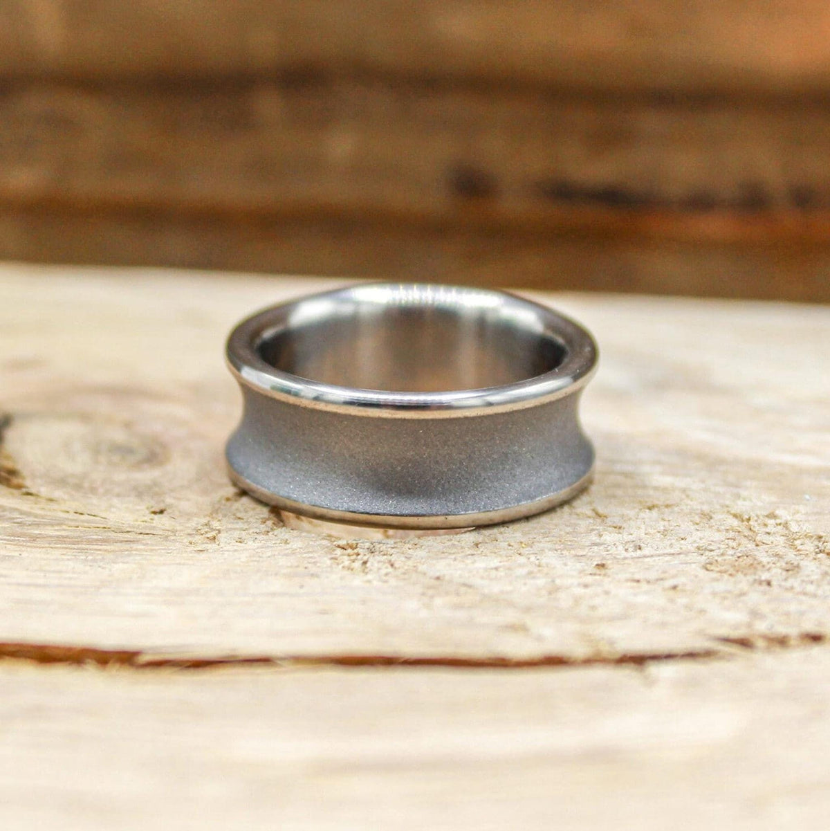 A silver-toned ring with a concave, sandblasted center and polished edges, viewed from the front on a light wood surface.