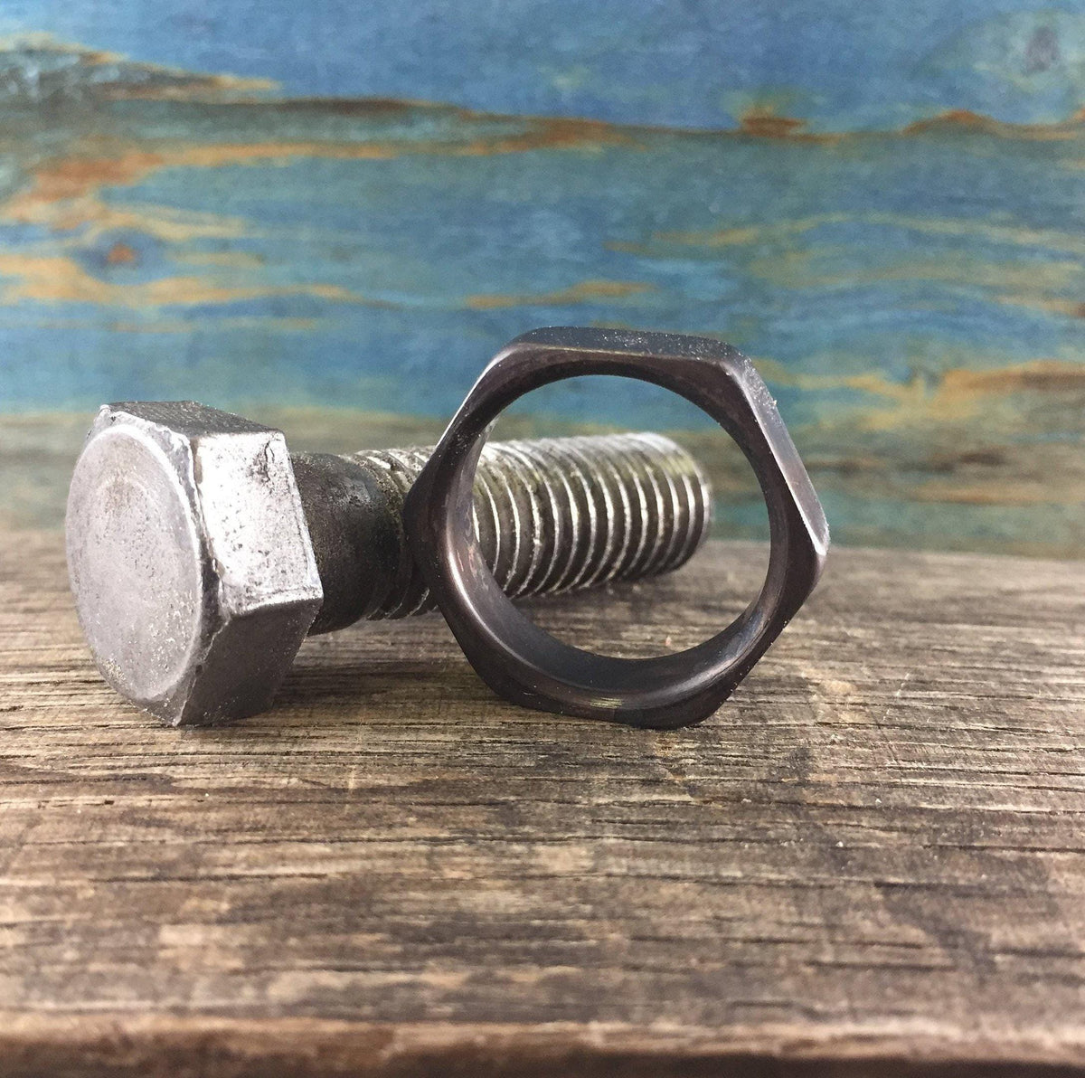 A dark hexagonal ring is positioned next to a large, rusty metal bolt on a wooden surface, viewed from the side.