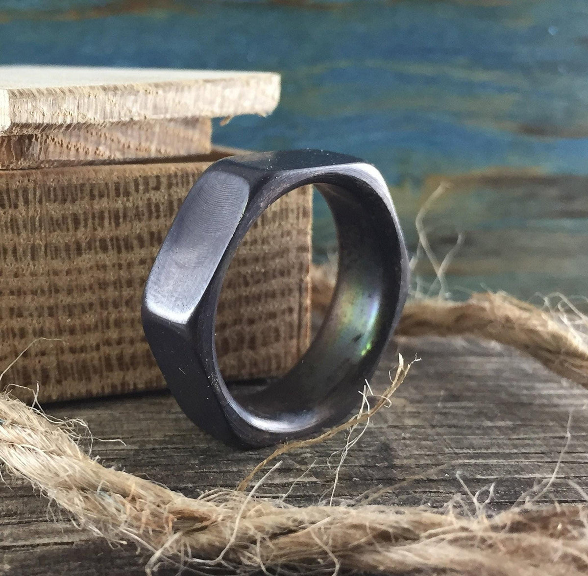 A dark hexagonal ring sits on a wooden surface next to a coil of twine and a stack of light wood blocks.