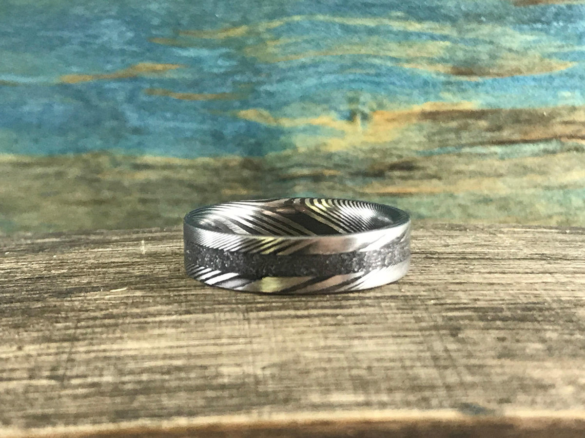 A silver-toned ring with a central textured band and patterned sides is centered on a wooden surface.