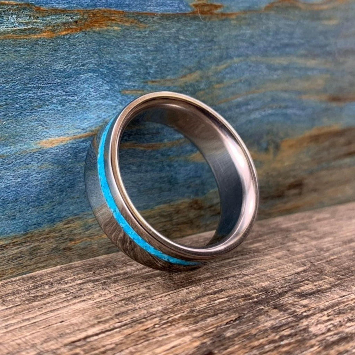 A silver-colored ring with a turquoise inlay, shown at a slight angle on a wooden surface.