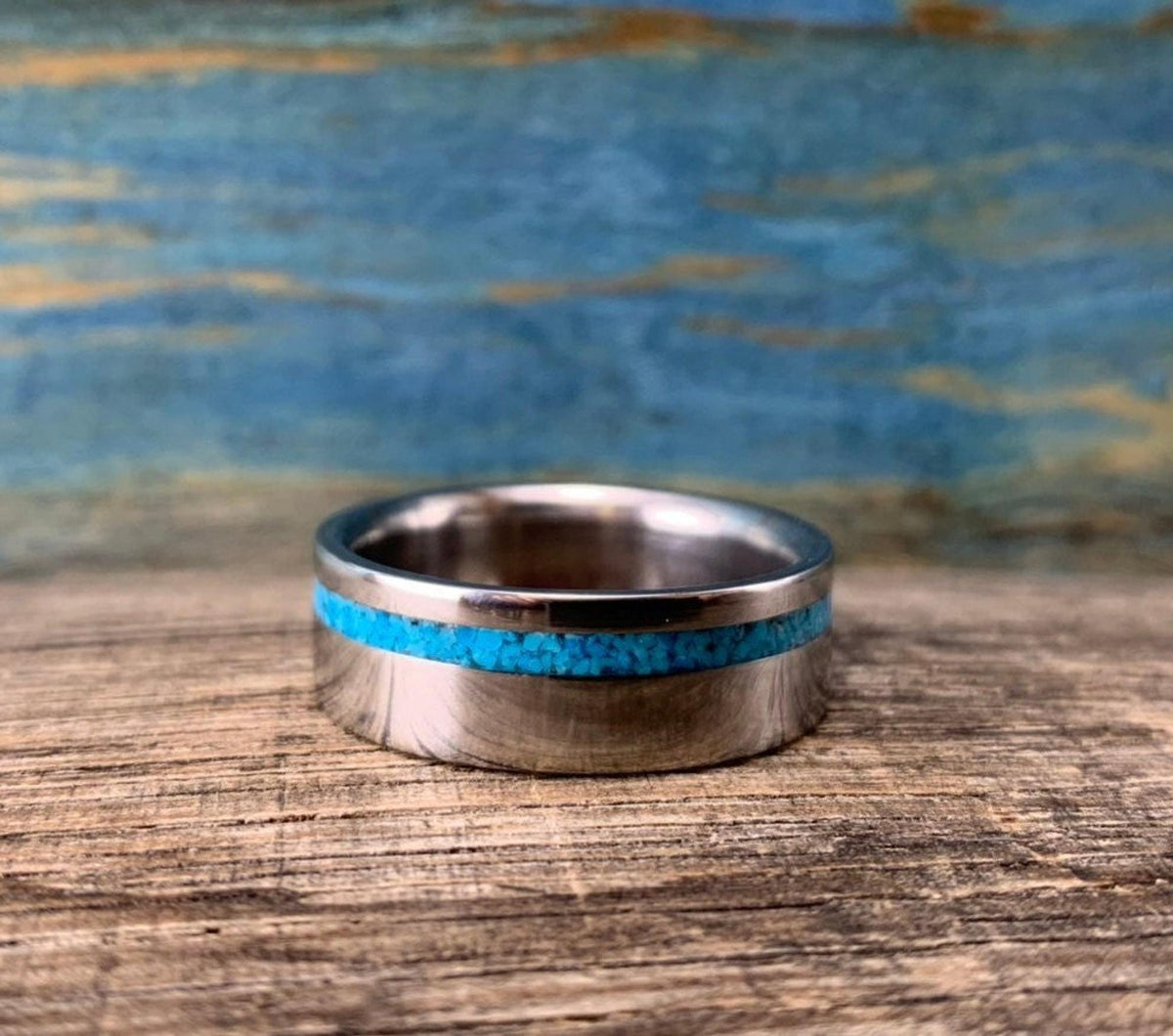 A silver-colored ring with a turquoise inlay, viewed from the front on a wooden surface.