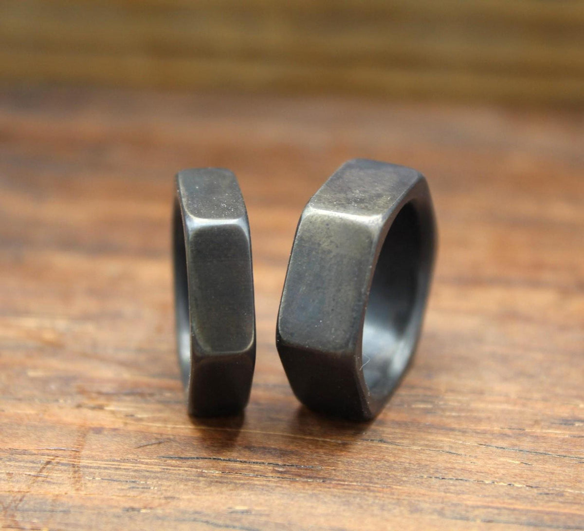 Two dark gray hexagonal rings, viewed from the side, standing upright on a wooden surface.