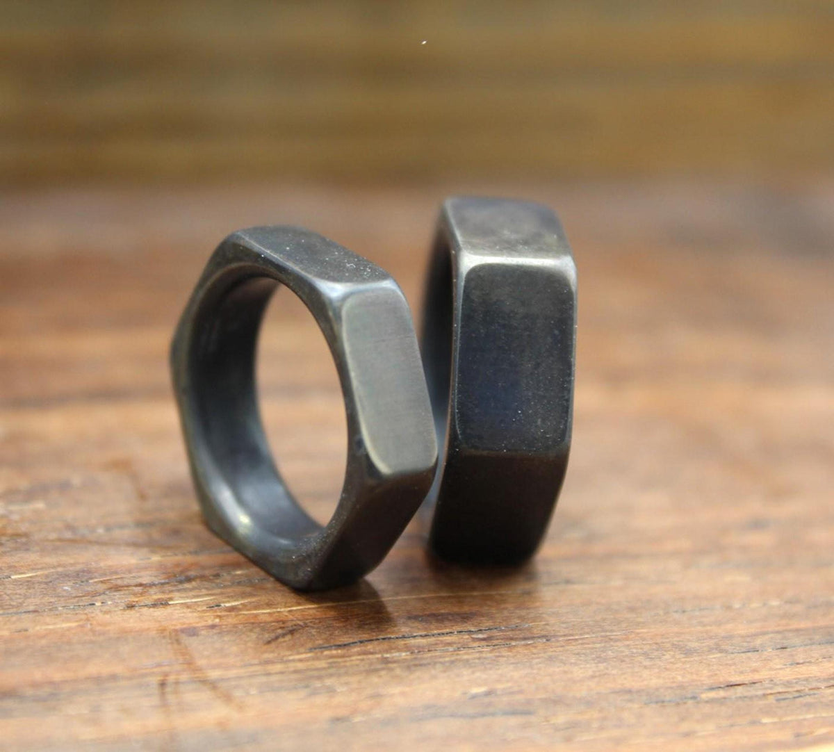 Two dark gray hexagonal rings, one slightly in front of the other, standing upright on a wooden surface.