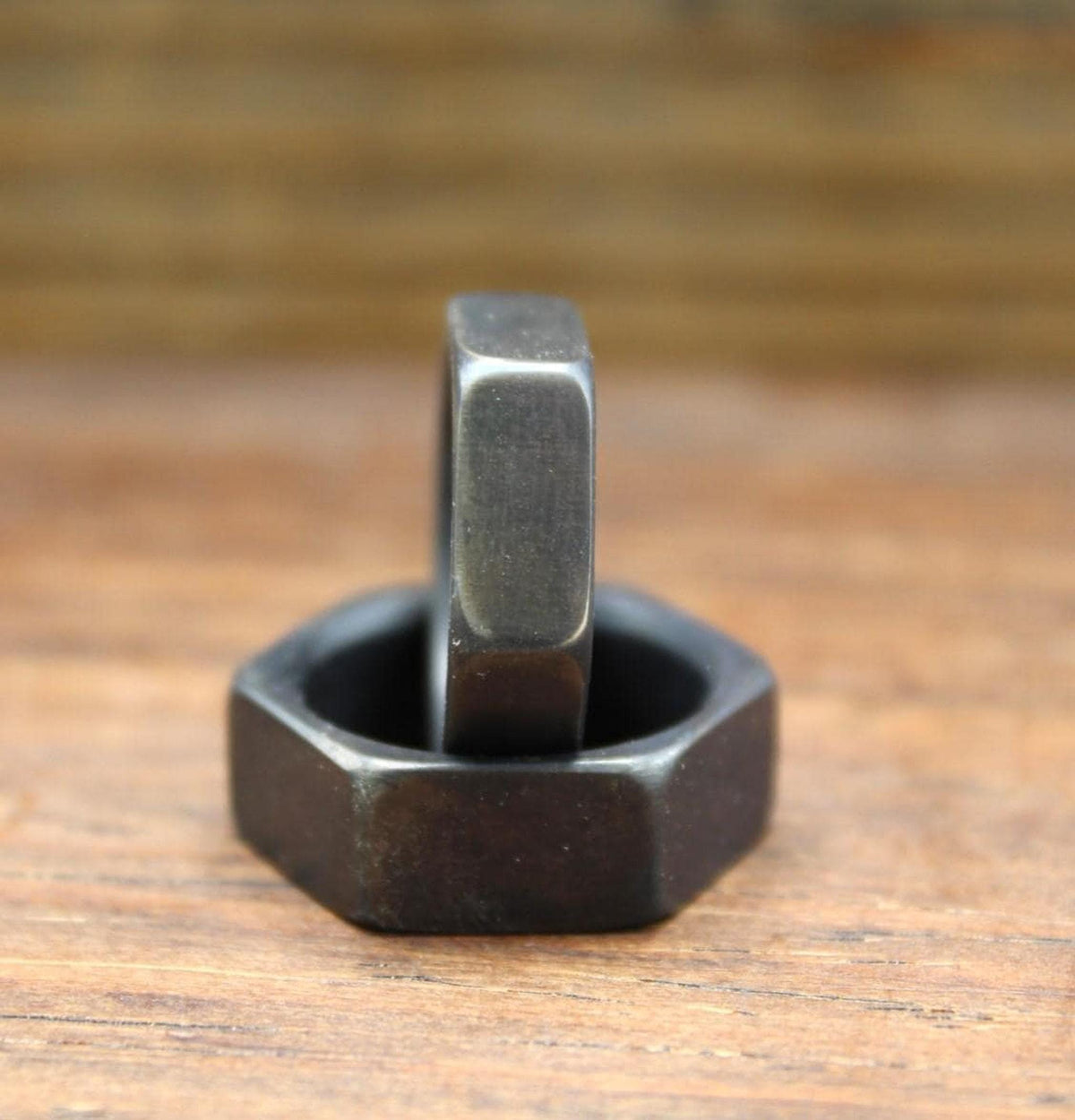 One dark gray hexagonal ring standing inside another dark gray hexagonal ring, on a wooden surface.