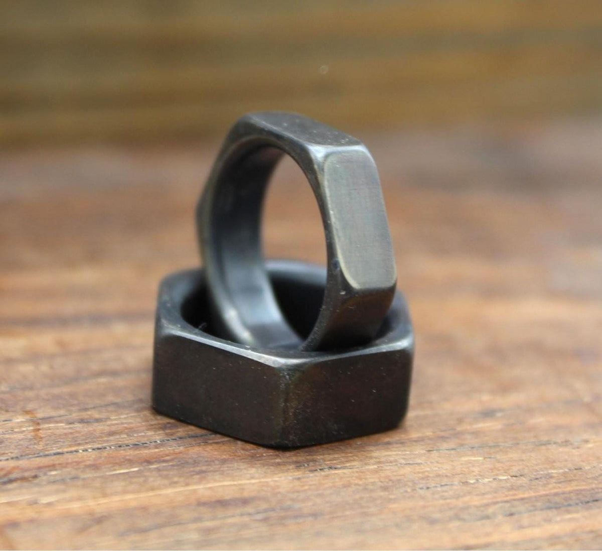 One dark gray hexagonal ring resting on top of another dark gray hexagonal ring, on a wooden surface.